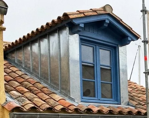 Lucarne habillée de zinc avec fenêtre bleue sur une toiture en tuiles canal à Martigues